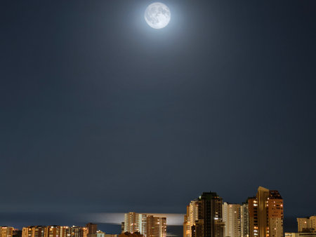 A breathtaking cityscape, magnificently illuminated by a full moon shining brilliantly in the night skyの写真素材