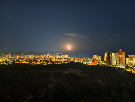 An absolutely stunning view showcasing a vibrant city skyline, beautifully illuminated at night by a rising moonの写真素材