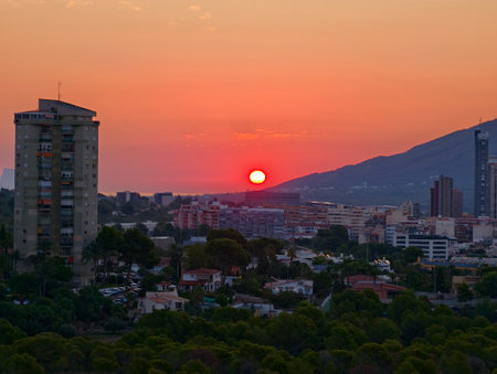 A beautiful sunset casts a warm glow over the city skyline and the nearby mountains in the backgroundの写真素材