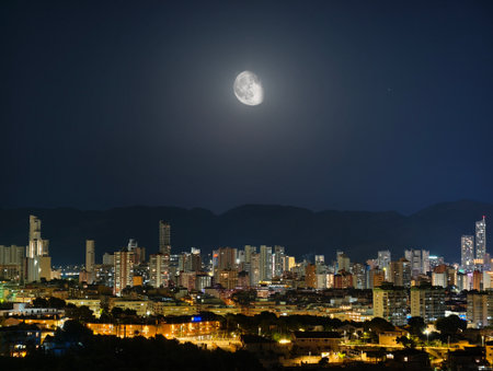 A truly breathtaking night view of a vibrant city beautifully illuminated by a stunning full moon overheadの写真素材