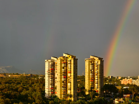 vivid highrises and rainbow arc, cityscape featuring tall structures beneath colorful rainbow arcの写真素材