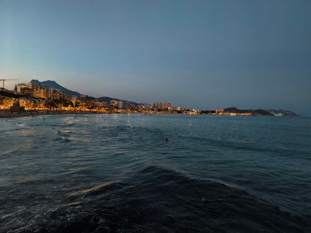 dusk coastal seascape, tranquil coastal bay at dusk reflecting distant city and mountain silhouettesの写真素材
