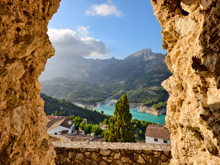 scenic mountain reservoir with village, archway reveals serene landscape of reservoir and mountainsの写真素材