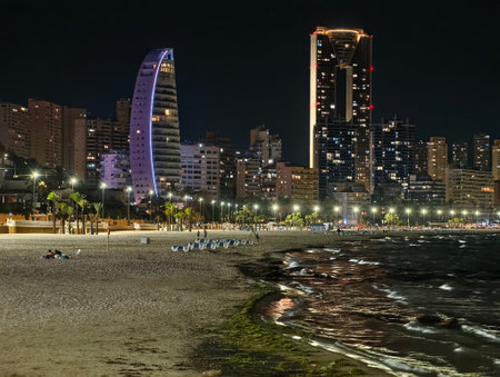 night beach scene, quiet beach under purplelit skyscraper with shimmering waterfront reflectionsの写真素材