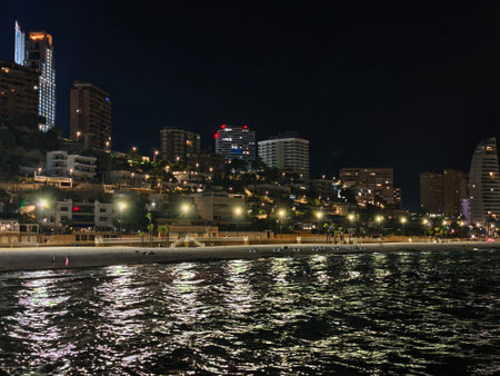 luminous coastal evening scene, reflections shimmer as gentle waves touch rocky shoreline at nightの写真素材