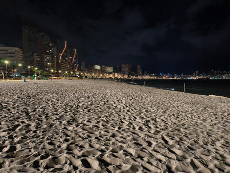 serene coastal scene, nighttime shoreline with city lights, tranquil beach illuminated by city glowの写真素材