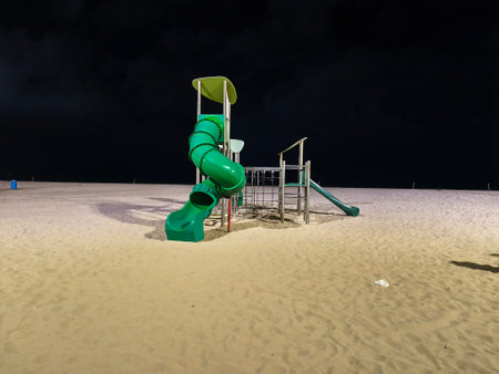 eerie quiet beach with playground at night, lone green spiral slide on quiet beach at nightの写真素材