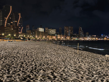 seaside view with city lights, coastal nighttime scenery with urban illumination and textured sandsの写真素材