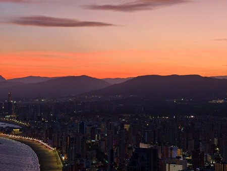 sunset over city with mountains afar, dusk illuminates skyline with glowing city lightsの写真素材