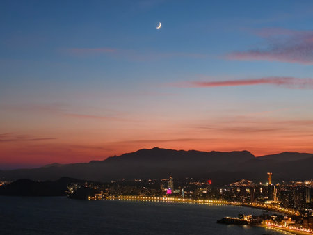 urban planner examines nightlight patterns against calming bay and distant mountain silhouettesの写真素材