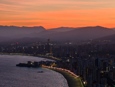 nightlife hub with waterfront and mountains, clustering highrises by shimmering bay at duskの写真素材
