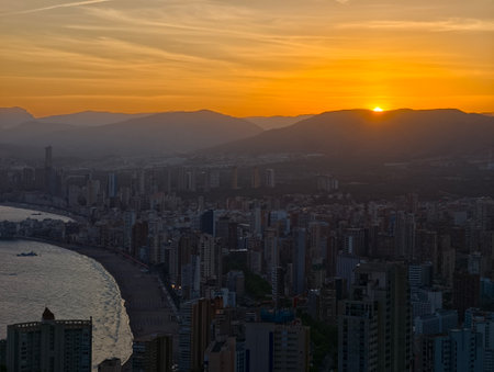warm sunset beyond skyline, drone captures glowing sunset behind highrises and distant mountainsの写真素材
