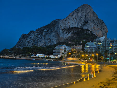 calm oceanfront scene at twilight featuring towering rocks and shimmering city reflectionsの写真素材