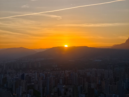 contrails and city skyline at sunset, sunset over city with aircraft trails and mountain backdropの写真素材