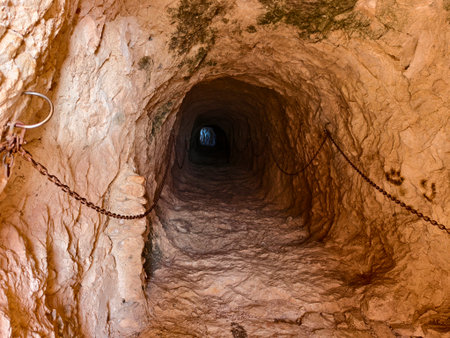 dark rocky tunnel featuring weathered chains hanging, gloomy rocky tunnel with aged chains hangingの写真素材
