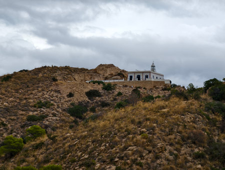 chapel in hills, serene hilltop chapel with winding access amidst rugged terrain and cloudy skyの写真素材