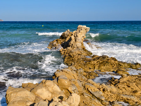 serene rocky coast under sunlight and waves, calm coastal rocks with shifting tides and shadow playの写真素材