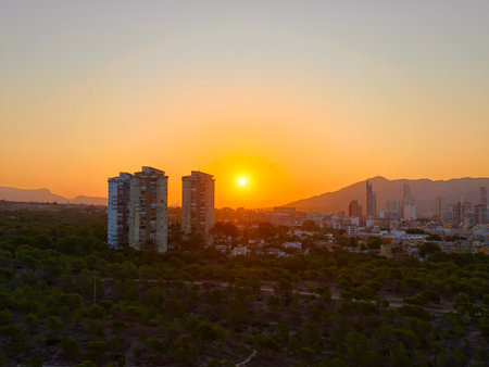 evening scene featuring sunset illuminating twin residential buildings with city skyline backdropの写真素材