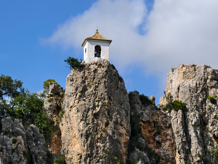 serene white bellhouse situated on solitary rock spire with mountain panorama in backgroundの写真素材