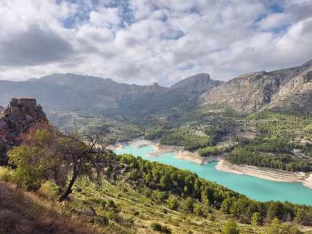 mountain peaks shrouded in clouds above vivid turquoise lake under dramatic light conditionsの写真素材