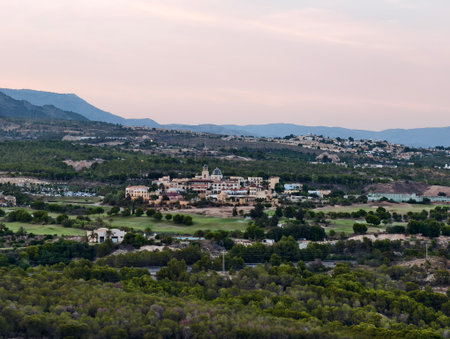 A stunning aerial view showcasing vibrant greenery, a charming village, and majestic distant mountainsの写真素材