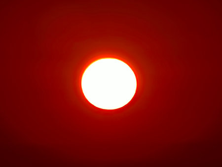 A view of the sun setting against a fiery red sky, creating a dramatic and mesmerizing ambianceの写真素材