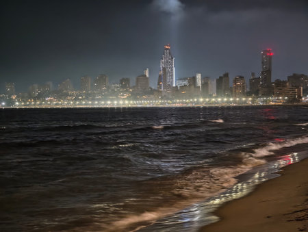 City lights and ocean waves, Silent night scene with towering lighthouse framing shimmering reflections on wet sandsの写真素材