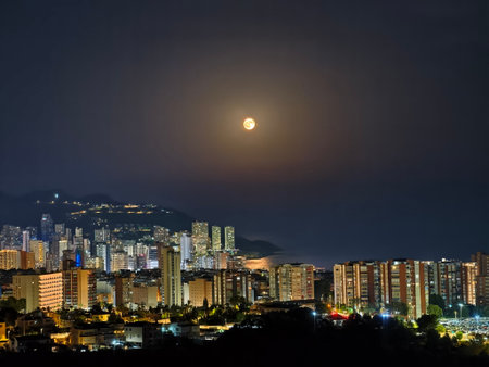 Town skyline viewed at dusk, Nighttime cityscape illuminated by moon, Settling dusk over urban horizon with glowingの写真素材