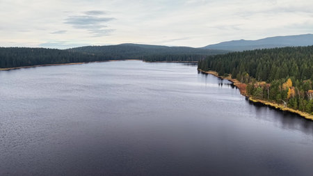 Quiet water scene surrounded by trees and hills, Tranquil aerial shot showcasing calm waters and distant mountainsの写真素材