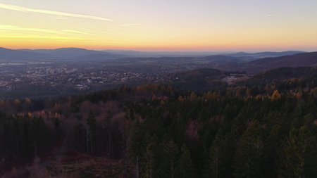 ranger surveys horizon at dusk, serene evening vista with rolling hills and twinkling village lightsの写真素材
