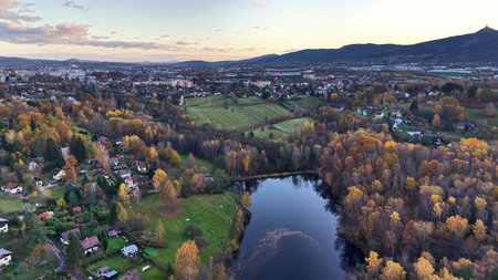 twilight hue reflects on peaceful pond, serene sunset view with lush fields and distant settlementsの写真素材