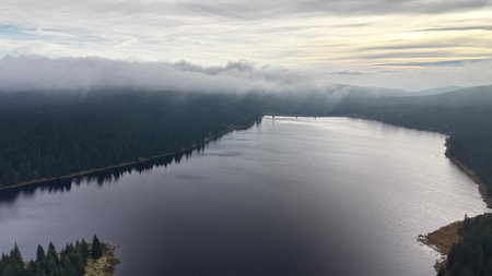 peaceful remote landscape featuring mirrorlike lake surrounded by dense fog and overcast skyの写真素材