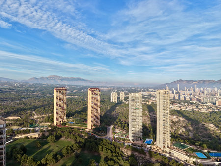 sunlit towers beside rolling green hills, expansive blue sky with cirrus clouds, soft shadows across lawnsの写真素材