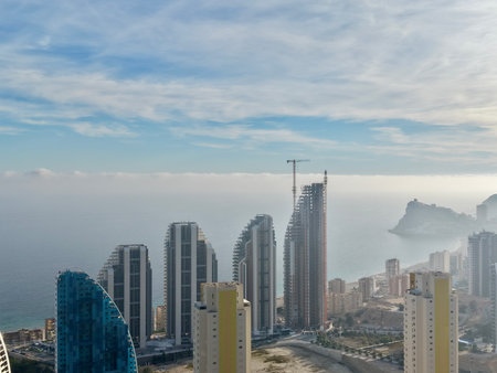 misty seafront highrise cluster with soft haze over sea and rock outcrops, muted tones and calm water createの写真素材