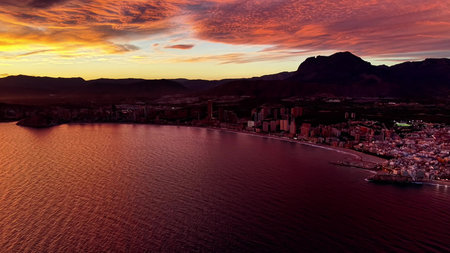 crimson twilight over coastal city, panoramic aerial reveals lit streets, harbor edge and mountain...
