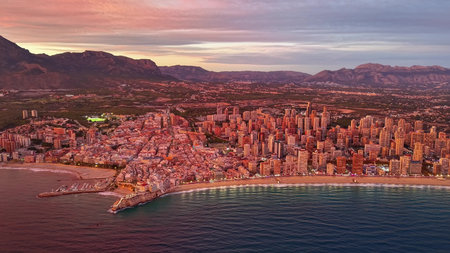 aerial view coastal city at sunset with illuminated beachfront and mountain backdrop