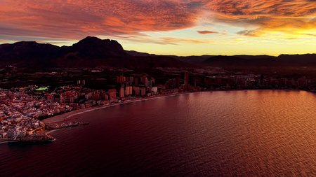 sunset coastal city with dramatic sky and glowing bay, mountain silhouette, reflective water and illuminatedの写真素材