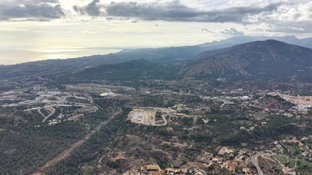 Aerial mountain view toward coastline with sprawling suburbs and winding roads, layered ridgelines...