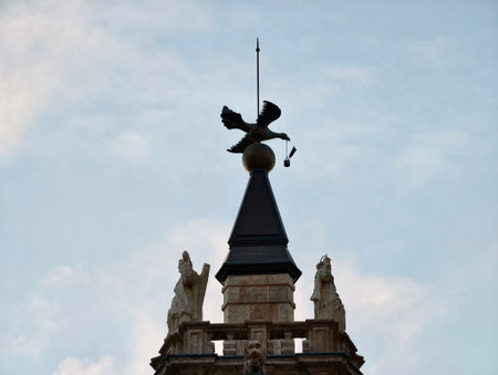 rooftop statues surrounding conical spire silhouette with decorative wind vane, cloudy sky backdrop,の写真素材