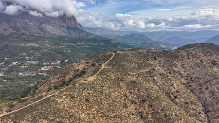 Mountain trail winding along ridge under cloud deck, ranger patrol perspective with rugged path, sweepingの写真素材