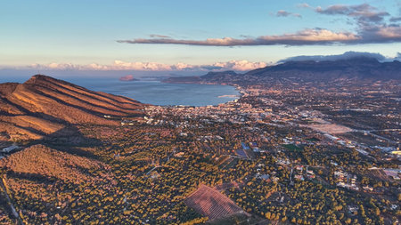 Sunlit ridge overlooking coastal city bay during golden hour, warm shadows sculpt slopes, urban gridの写真素材