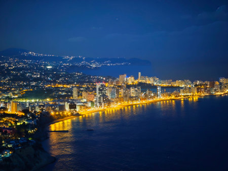 Evening skyline with waterfront glow stretching along curved bay, continuous ribbon of lights outlines shore,の写真素材