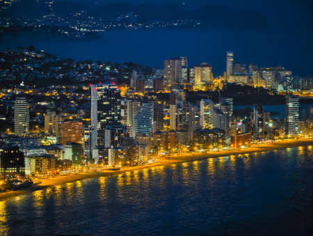 Seaside highrise boulevard glowing at night, bright lines of traffic and streetlights trace coastal...