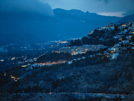 Twilight mountain village lights glow, soft blue tones with warm window illumination, winding road threadingの写真素材