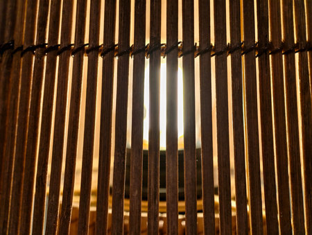 Sunlight streaming through vertical wooden slats, warm amber glow, narrow gaps creating dramatic shadows,の写真素材