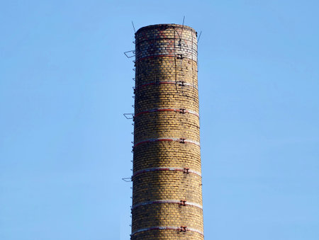 Decommissioned brick smokestack standing against sky, metal anchors around circumference, no smoke, quietの写真素材