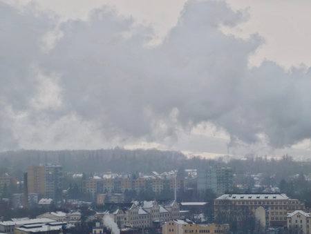 Dense smog blanketing urban skyline and factory plumes, low visibility across rooftops, muted tonesの写真素材