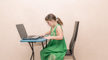 Concentrated styled little girl sitting behind a table and doing her computer home work