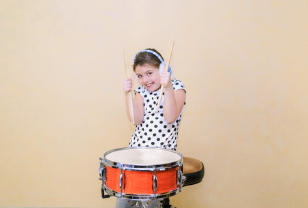 Little happy joyful girl in motion sitting behind the snare drum and holding a sticks against Tuscan sun venetian plaster wall backgroundの写真素材