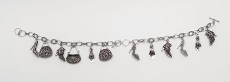 Open silver bracelet isolated on a grayish background with miniature pendants